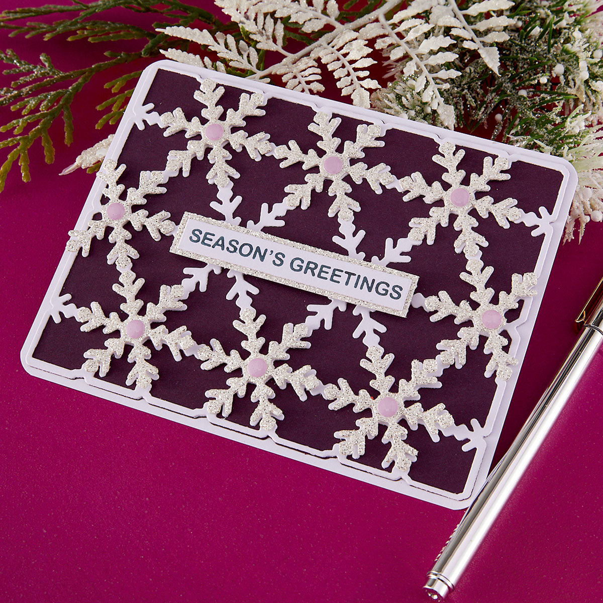 Season's Greetings card with snowflake design on a pink background