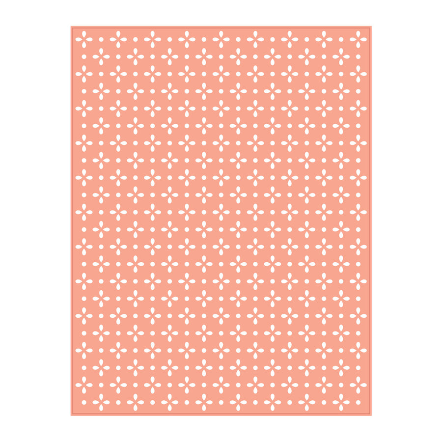 A rectangular sheet of white cardstock or paper featuring a repeating pattern of small white floral or cross-like motifs on a soft peach-pink background, shown against a plain white backdrop. Spellbinders Quilted Etched Dies by Simon Hurley