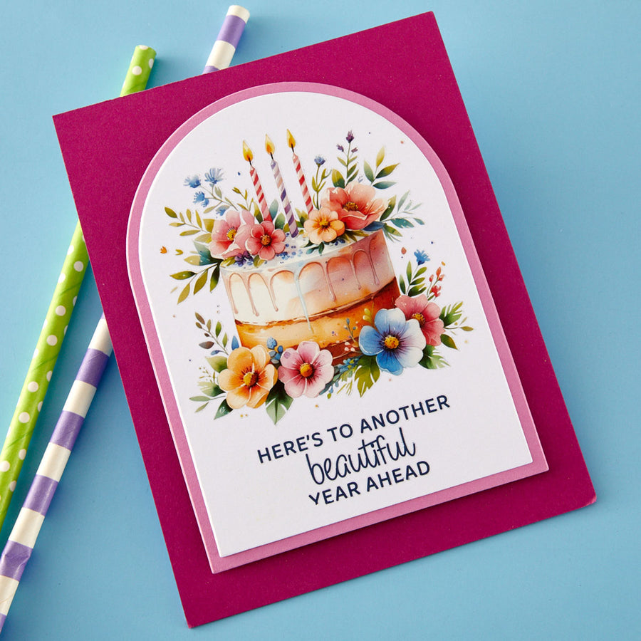 Handmade greeting card showing a birthday cake with candles and decorated with flowers. Sentiment says 'Here's to another beautiful year ahead'