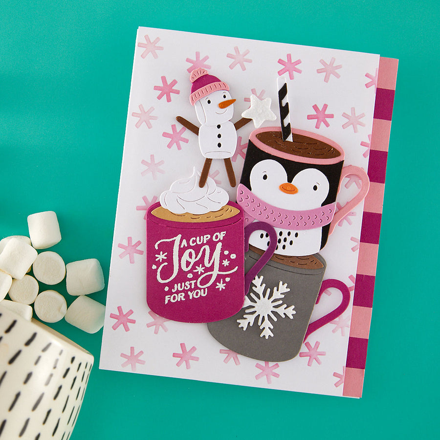 A handmade holiday greeting card featuring cartoon penguins and a snowman with hot cocoa cups, styled on a teal background with marshmallows and a ceramic mug from Spellbinders using the Mug Friends Etched Dies and the Spellbinders Snow Joy Stencil