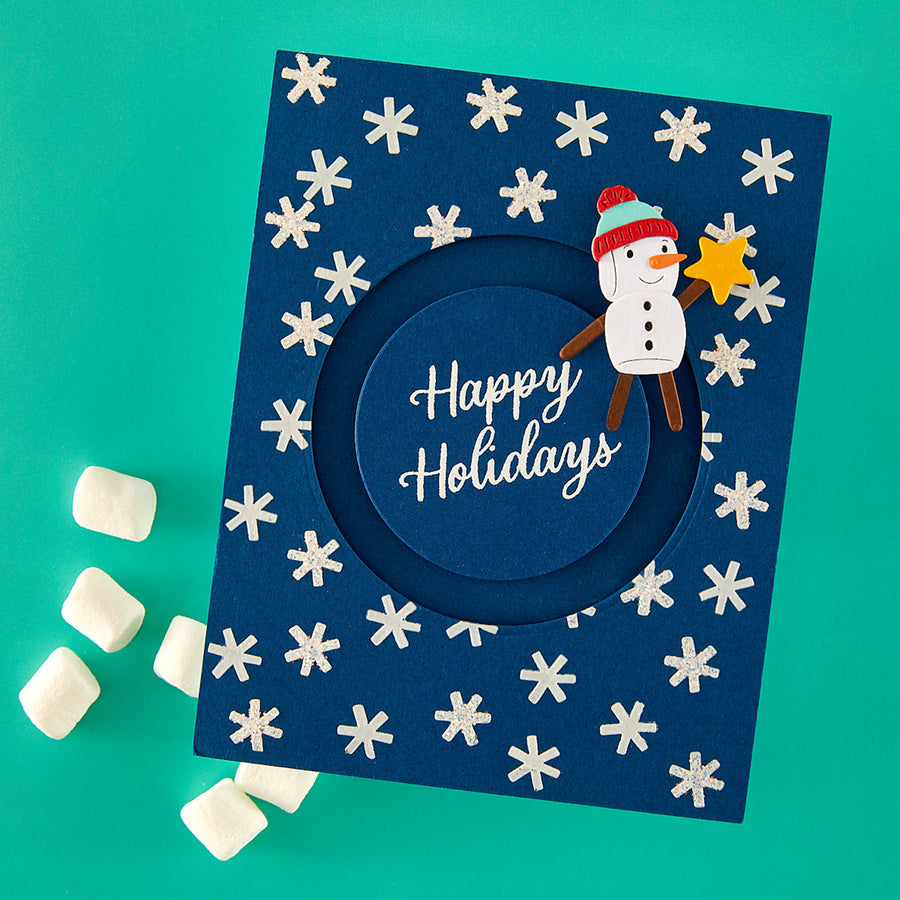 A handmade navy blue handmade holiday card with a circular cutout in the center and the words 'Happy Holidays' in white script. The card is decorated with white snowflakes and features a paper snowman wearing a red and green hat and brown arms, holding a yellow star. Spellbinders Mugs and Kisses Sentiments Clear Stamp Set