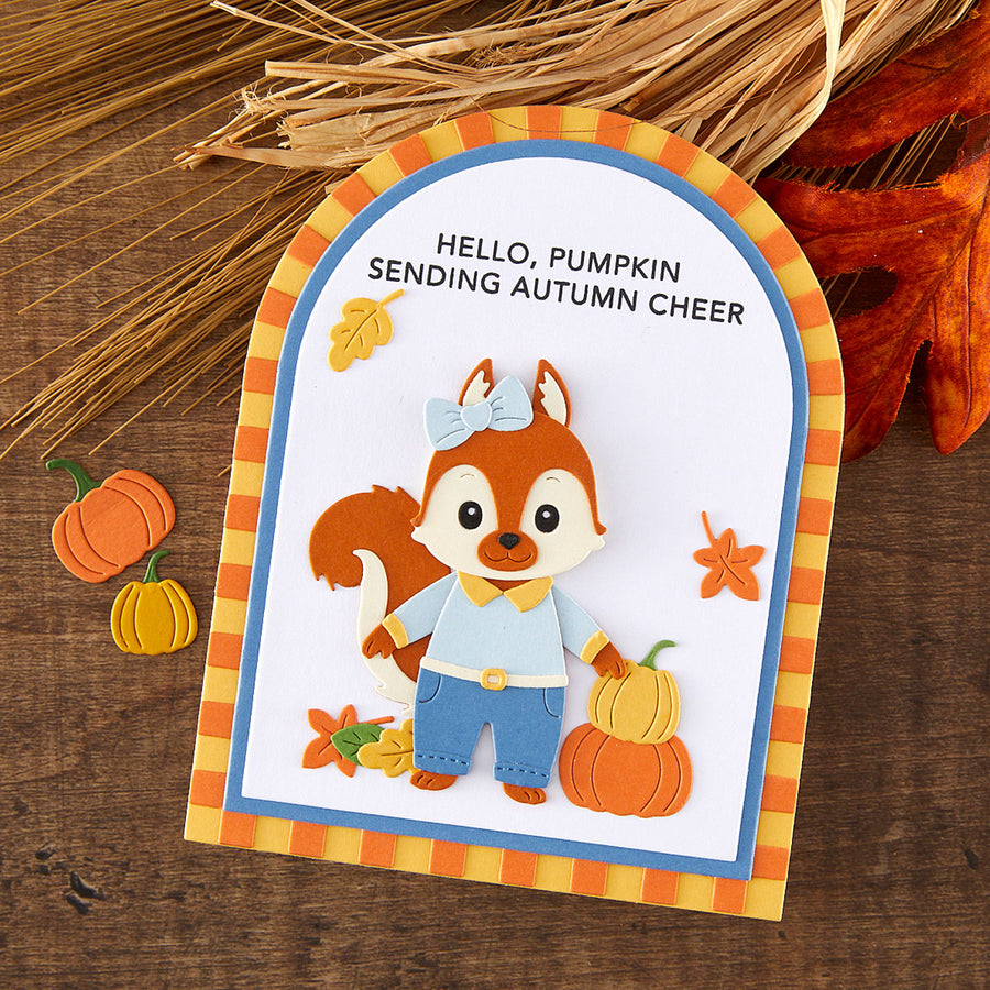 A handmade autumn-themed card featuring a layered paper fox character wearing blue pants and a light blue shirt, holding a small orange pumpkin. The card has a blue and orange striped border and reads 'HELLO, PUMPKIN SENDING AUTUMN CHEER'.