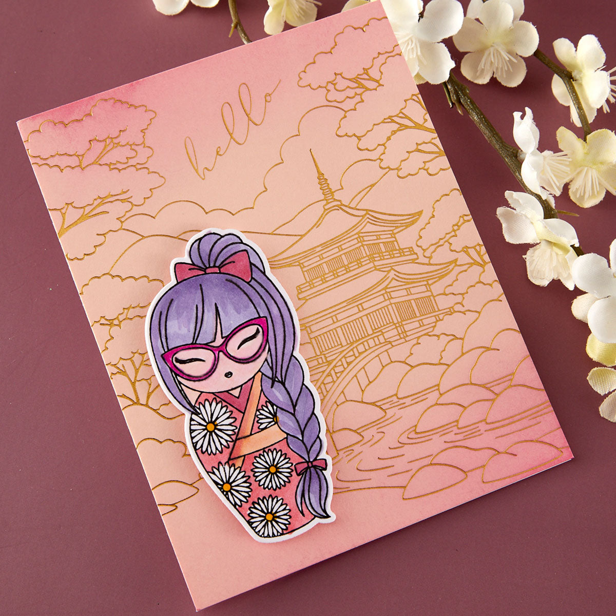 A pink and peach Japanese-themed card with gold foil line art of a pagoda and cherry blossoms, featuring a die-cut sticker of a purple-haired girl in a floral kimono on the front, styled with white flowers on a mauve background.