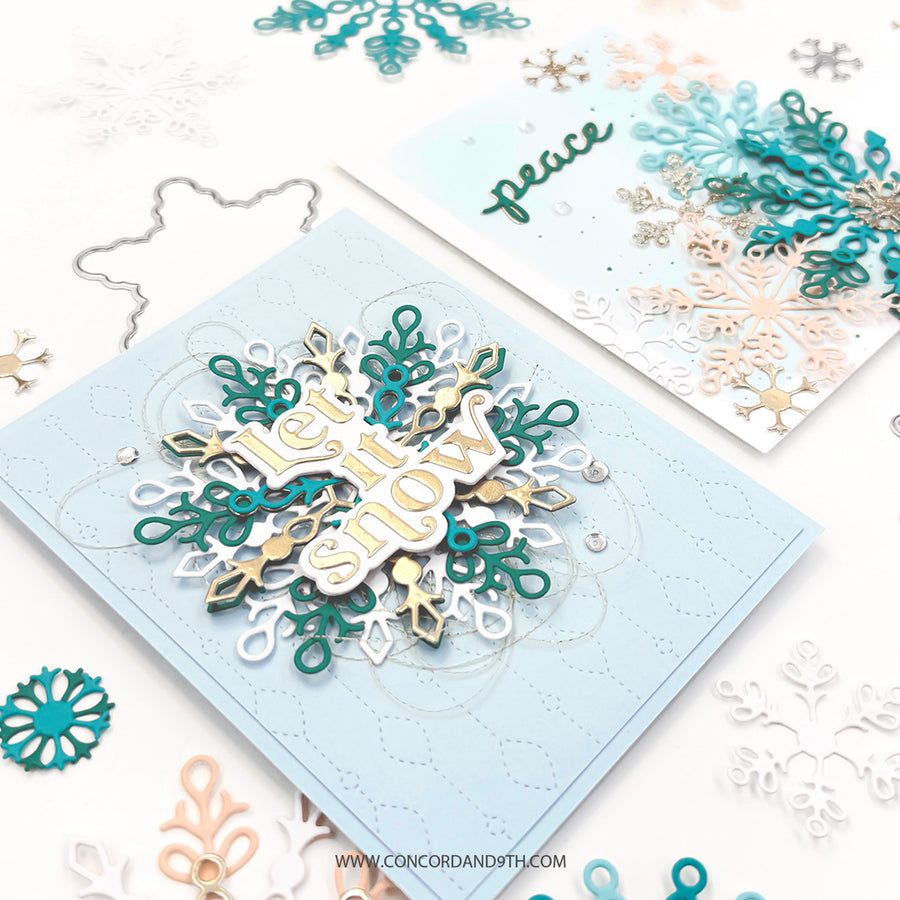 A handmade layered card featuring a large snowflake design with the words 'let it snow' in white, teal, and gold, displayed on a light blue card. A second card in the background shows a similar design with the word 'peace' in teal.