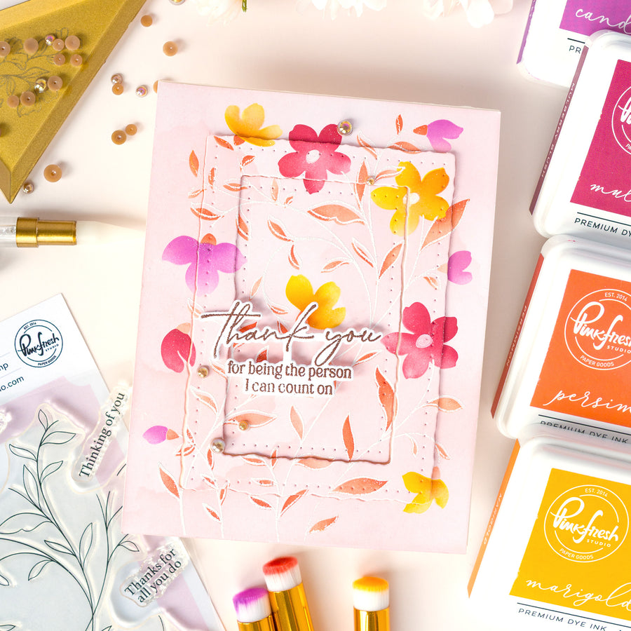 A handmade thank you card with layered pink floral frames and the text 'thank you for being the person I can count on!' surrounded by craft supplies, including Pond's ink pads and stamping tools on a light pink background.