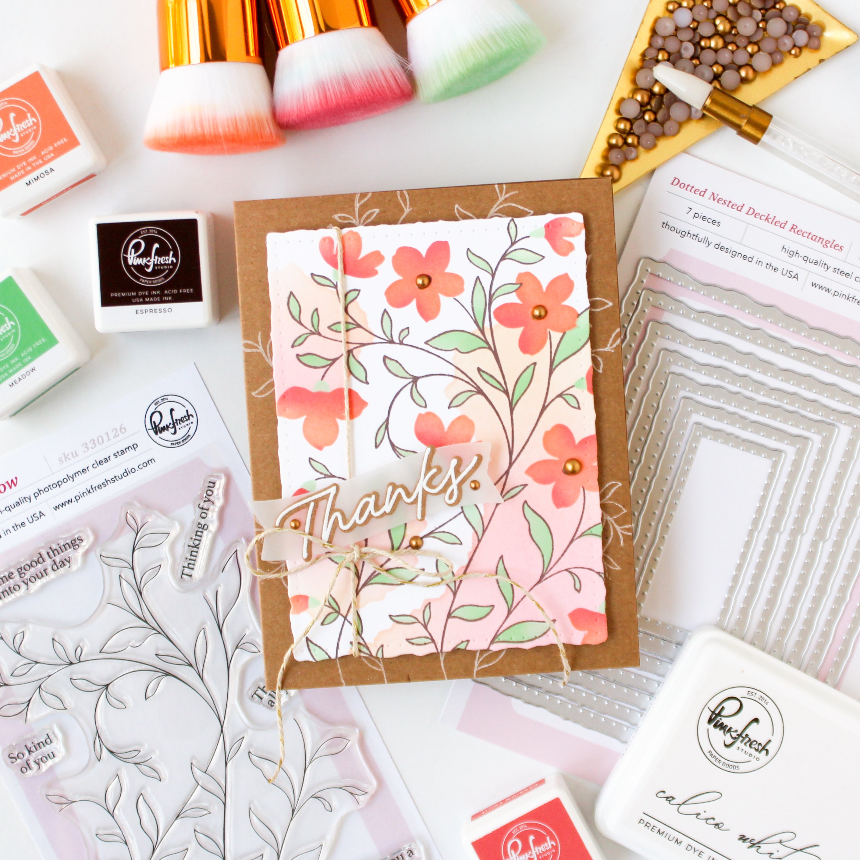 Floral card with 'Thanks' text surrounded by stamping supplies on a white background