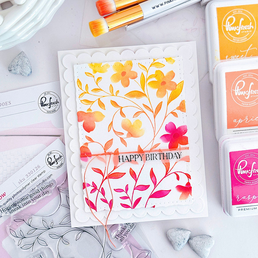 Floral birthday card with stamping supplies on a white surface