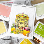 A handmade layered card featuring a yellow honey jar and lemons with the words 'Gratitude Blend' and 'Honeycomb Jar,' surrounded by Ranger Press premium dye ink pads in yellow, green, and pink tones.