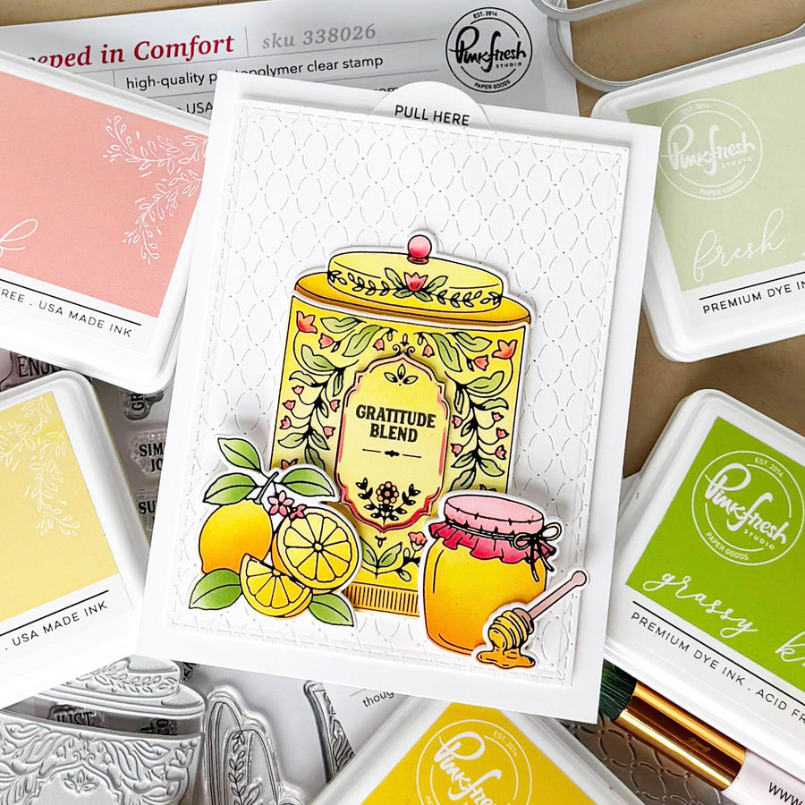 A handmade layered card featuring a yellow honey jar and lemons with the words 'Gratitude Blend' and 'Honeycomb Jar,' surrounded by Ranger Press premium dye ink pads in yellow, green, and pink tones.