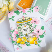 A handmade greeting card featuring a colorful illustration of honey jars, lemons, and pink flowers with the text 'SUNSHINE BLEND'. The card is styled on a white surface with crafting tools and flowers in the background.