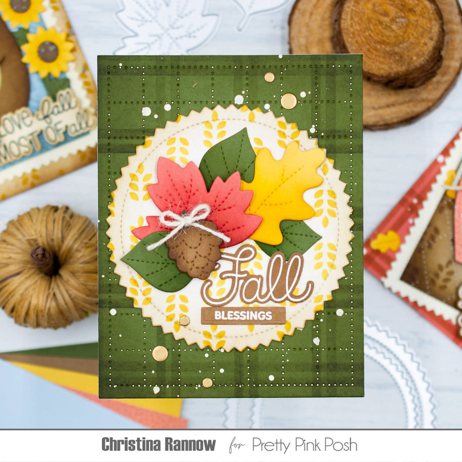 A handmade autumn-themed greeting card featuring a green plaid background, a scalloped cream circle with layered red and yellow fall leaves, acorns, and the words 'Fall Blessings'. The card is displayed on a light blue patterned surface with decorative autumn props and branding text at the bottom.