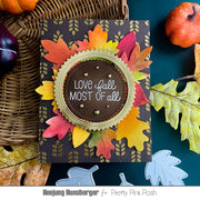A handmade autumn-themed greeting card featuring layered die-cut fall leaves in yellow, orange, pink, and green on a dark charcoal background. The center has a scalloped olive-green border around a brown circle with the phrase 'LOVE fall MOST OF all' in white script.