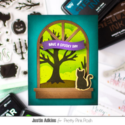 A handmade Halloween greeting card featuring a spooky tree silhouette, a black cat silhouette, and a purple banner reading 'HAVE A SPOOKY DAY' on a teal background, styled on a flat-lay surface with craft supplies.
