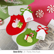 Two handmade Christmas stocking cards on a styled flat-lay background with peppermint candies and stamp sheets. One stocking is red with a silver glitter cuff and green bow, the other is green with a silver glitter cuff and red bow.