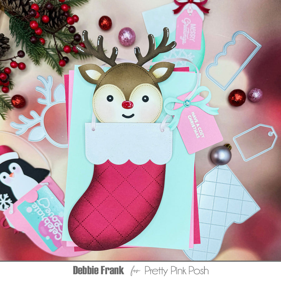 A festive Christmas handmade card featuring a reindeer peeking out of a pink stocking, surrounded by holiday decorations and tags. The text at the bottom reads 'Debbie Frank for Pretty Pink Posh'.