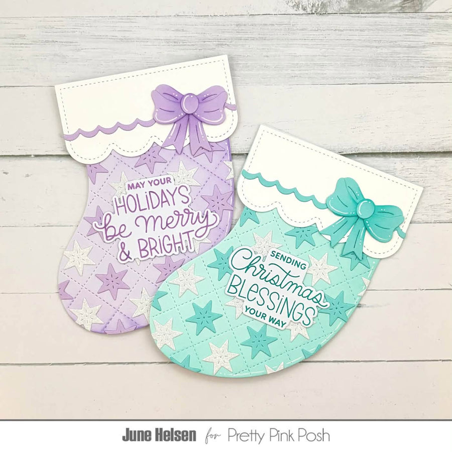 Two Christmas stocking-shaped handmade greeting cards or tags laid on a whitewashed wood surface. One is lavender with a purple bow and the text 'May Your Holidays Be Merry & Bright'; the other is mint green with a teal bow and the text 'Sending Christmas Blessings Your Way'.