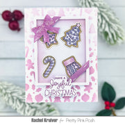 A handmade Christmas greeting card with a pink and white patterned border, featuring four illustrated holiday motifs inside a layered window: a bow, a decorated tree, a candy cane, and a stocking. The card reads 'HAVE A Joyful CHRISTMAS' and is photographed on a white wood surface with festive greenery and red berries around it.