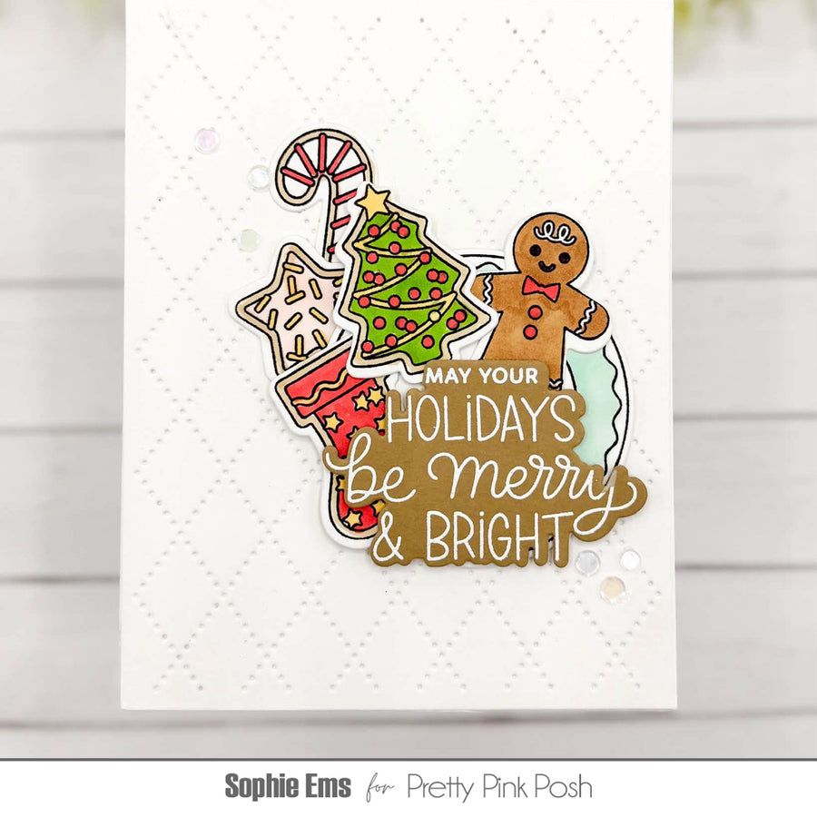 A handmade holiday greeting card featuring a layered die-cut design with a green Christmas tree, candy cane, gingerbread man, stocking, and the phrase “MAY YOUR HOLIDAYS be Merry & BRIGHT,” shown on a white embossed cardstock background.