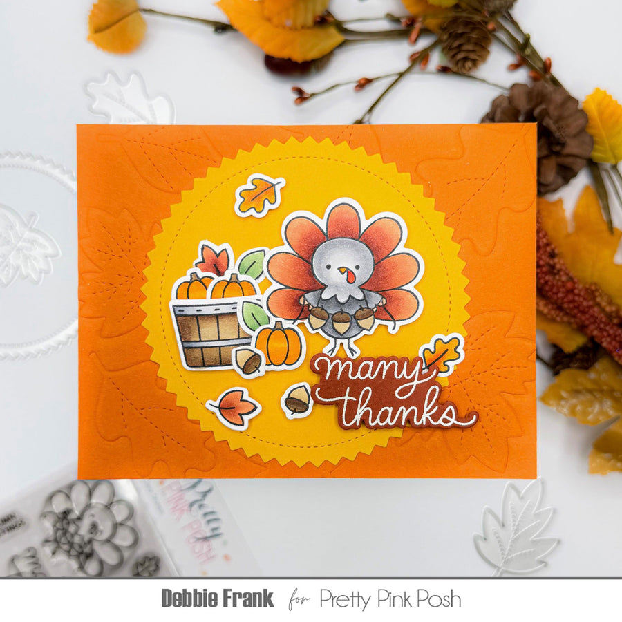 A handmade Thanksgiving-themed card featuring a cartoon turkey, pumpkins, acorns, and the words 'many thanks' on an orange background, styled with autumn leaves and decorative elements. Text at the bottom reads 'Debbie Frank for Pretty Pink Posh'.