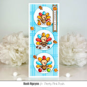 A handmade Thanksgiving-themed card featuring three cartoon turkeys with colorful feathers, pumpkins, autumn leaves, and a vertical banner reading 'HAPPY FALL' on a light blue plaid background. The card is photographed upright on a light surface with white decorative flowers blurred in the background.