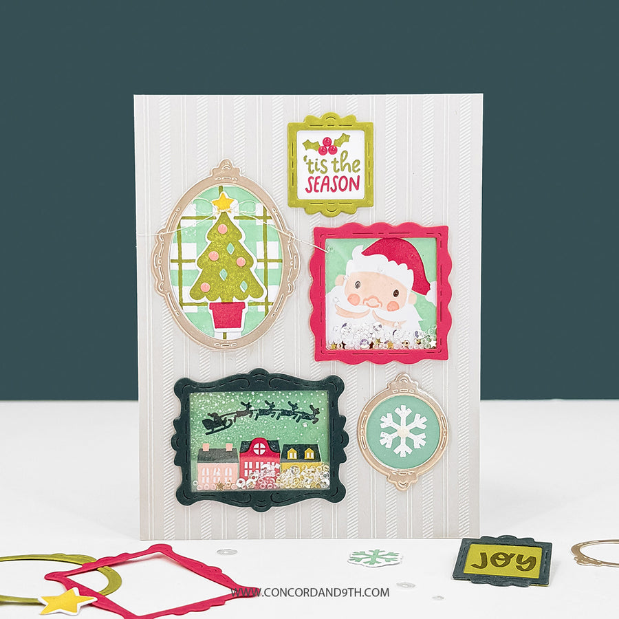 A handmade Christmas greeting card displayed on a white surface against a dark teal background. The card features layered die-cut frames with festive illustrations including a Christmas tree, Santa Claus, a snowflake, and a snowy house.