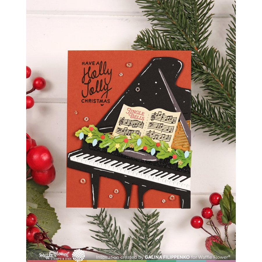 A handmade Christmas greeting card featuring a black grand piano with an open sheet music book, decorated with a green garland and red berries, set against a rust-orange background. The card is styled on a white wood background with pine branches and red berries.