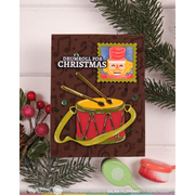 A handmade Christmas card featuring a red and gold drum with yellow drumsticks, set against a dark brown patterned background with the text 'DRUMROLL FOR CHRISTMAS' and a nutcracker illustration. The card is styled with pine branches, red berries, and small crafting tools on a white wood background.