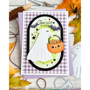 A Halloween-themed greeting card featuring a white dog ghost and a pumpkin candy basket, styled on a wooden surface with autumn leaves, scissors, and craft tools.