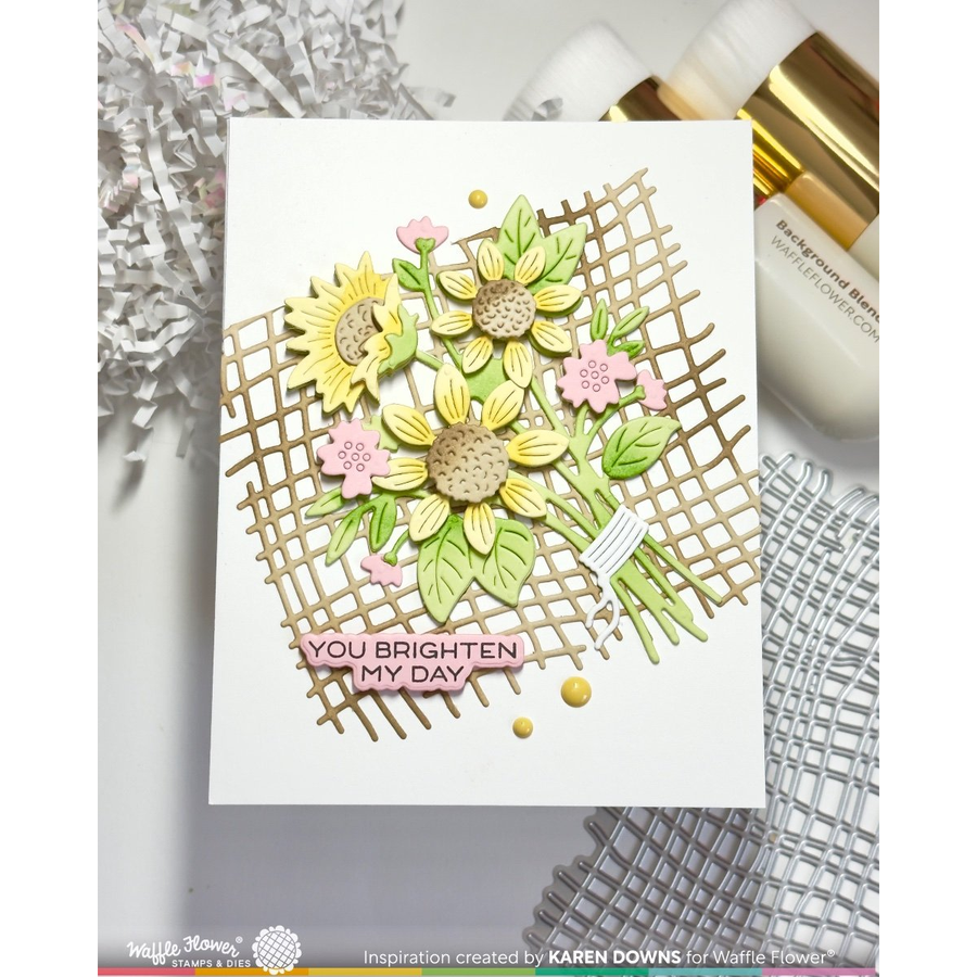 A handmade greeting card featuring a 3D sunflower bouquet with a gold die cut lattice design, pink cherry blossoms, and the text 'YOU BRIGHTEN MY DAY'. The card is styled on a white surface with craft supplies in the background.