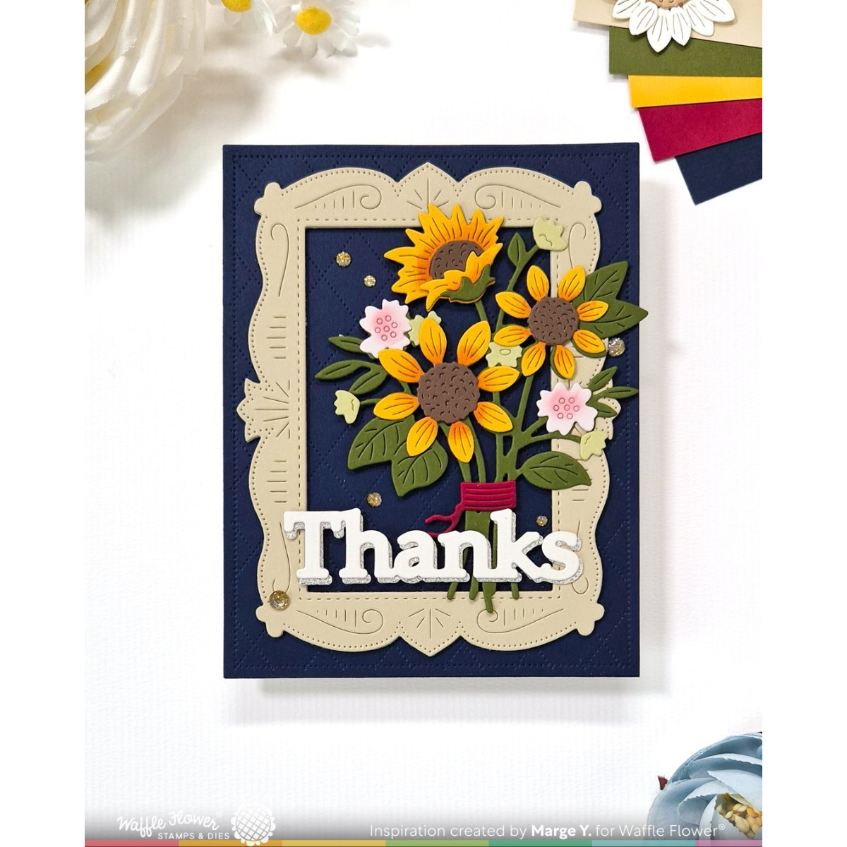 A handmade greeting card featuring a navy blue background, a cream-colored ornate frame, and a 3D sunflower bouquet with green leaves and pink flowers. The card is layered with a white 'Thanks' die-cut text element.