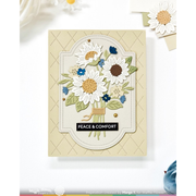 A handmade greeting card featuring a layered die-cut sunflower bouquet with green leaves, blue flowers, and a black banner reading 'PEACE & COMFORT' on a cream background.
