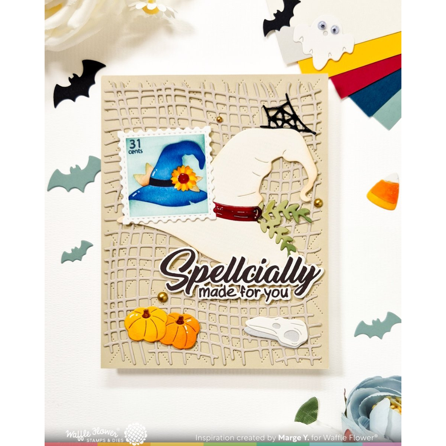 A handmade Halloween greeting card with a beige background, featuring a die-cut white witch hat, a blue witch hat stamp, orange pumpkins, black spiderweb details, and the text 'Spellically made for you'. The card is displayed on a white background with decorative paper ghosts, bats, and candy.