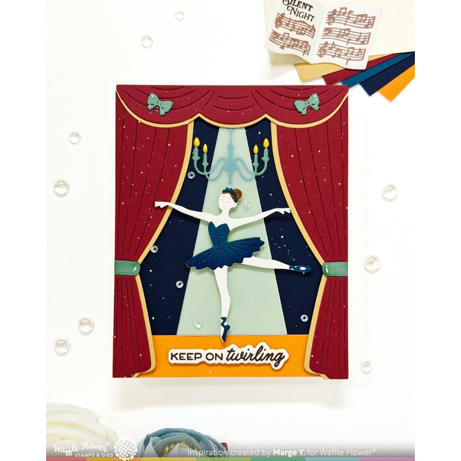 A handmade layered card featuring a ballet dancer in a blue tutu in front of red stage curtains, with the text 'KEEP ON twirling' at the bottom. The card is displayed on a white background with decorative bubbles and scrapbook elements.