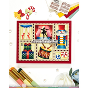 A handmade Christmas collage card featuring a red border and six festive stamp-like panels with a dancer, nutcracker, gifts, candy canes, and musical instruments. The card is displayed on a white background with craft props, including paper clips, markers, and a white rose.