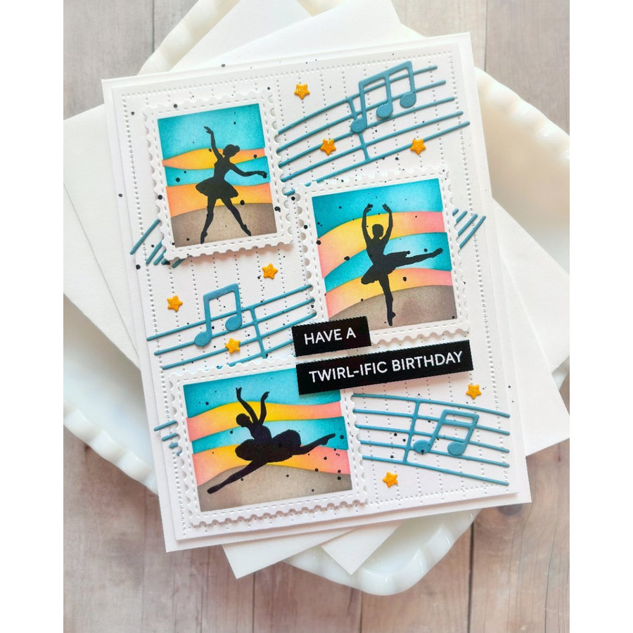 A handmade greeting card featuring three panels with ballet dancer silhouettes against a sunset gradient, decorated with blue musical notes and stars. The card has a black banner reading 'HAVE A TWIRL-IFIC BIRTHDAY' and is displayed on white paper sheets over a light wood surface.