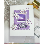 A handmade greeting card with a white base, featuring a layered purple stamp design with scalloped edges, white flower cutouts with pink centers, and the text 'you are the Best'. The card is displayed on a white surface with craft supplies in the background.