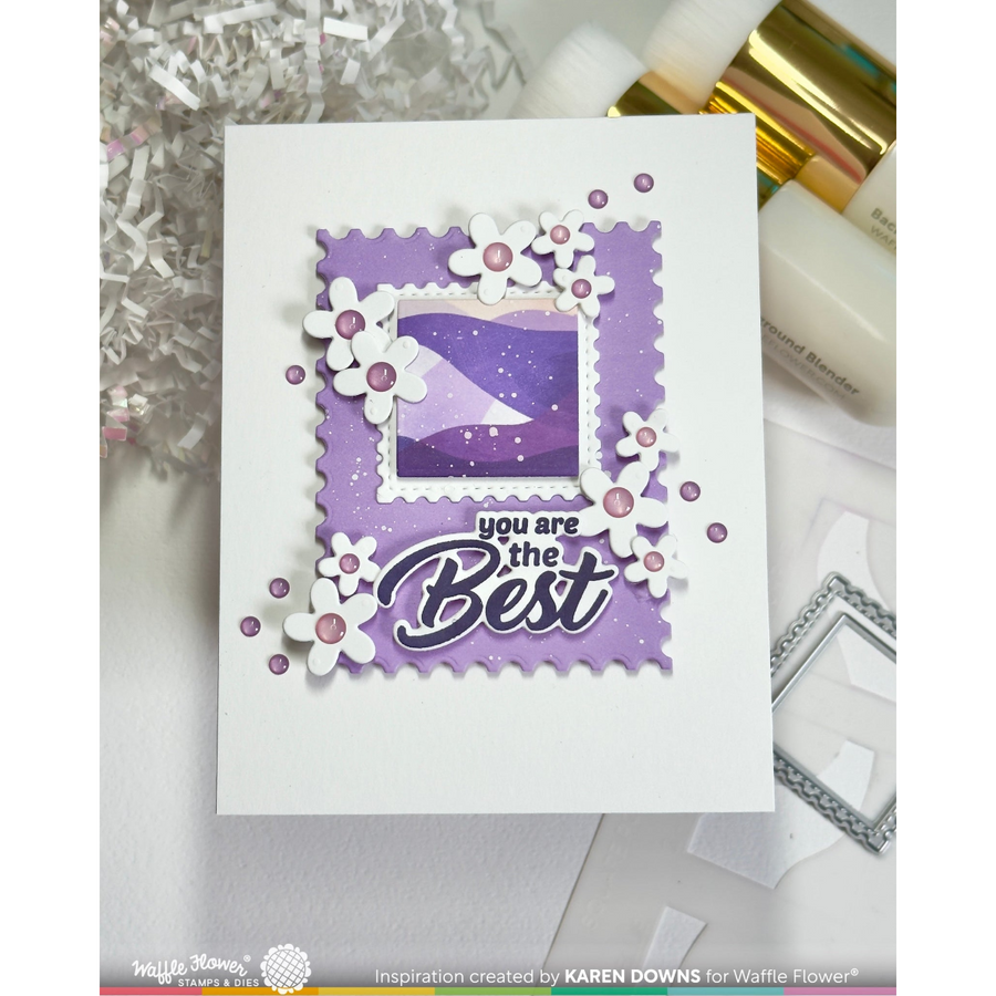 A handmade greeting card with a white base, featuring a layered purple stamp design with scalloped edges, white flower cutouts with pink centers, and the text 'you are the Best'. The card is displayed on a white surface with craft supplies in the background.