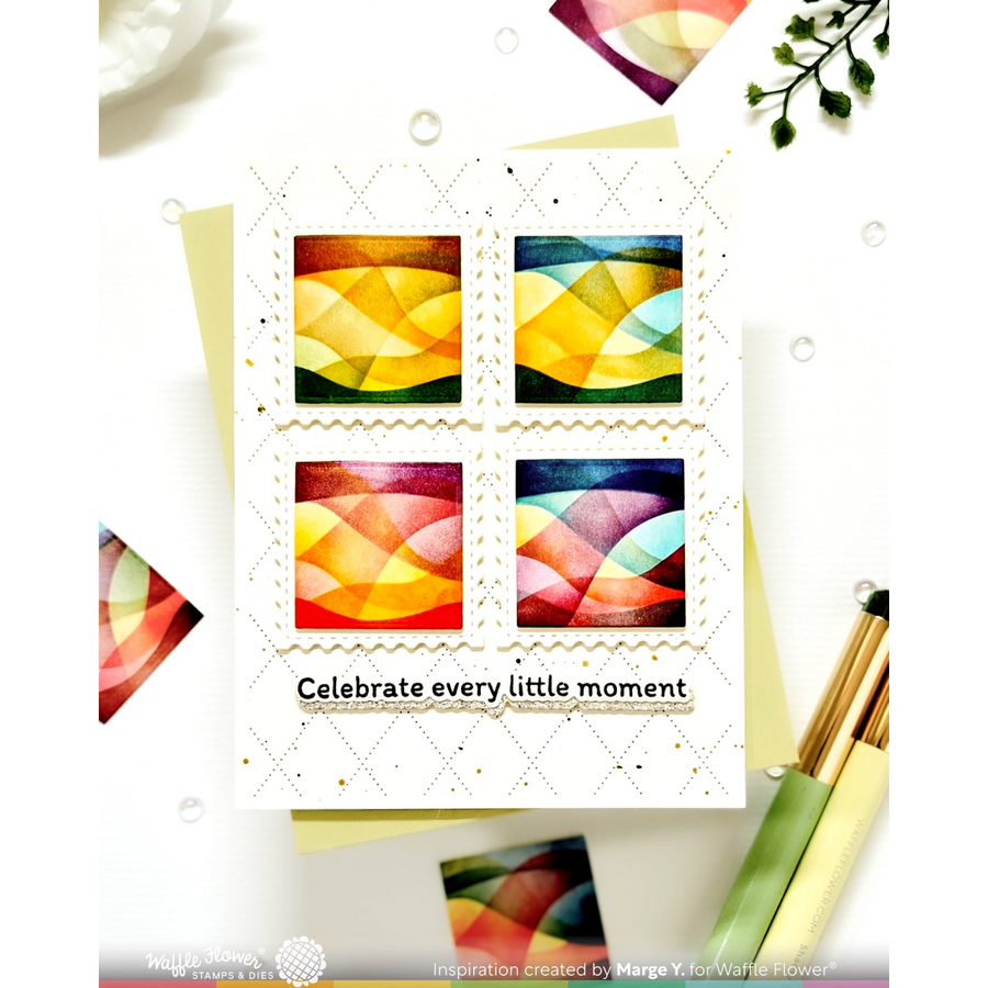 A handmade greeting card featuring four colorful abstract geometric stamps arranged in a 2x2 grid, with the text 'Celebrate every little moment' printed below. The card is styled on a white background with decorative paper scraps, paintbrushes, and small green leaves.