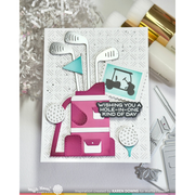 A handmade greeting card featuring a golf-themed design with a pink and white golf bag, golf clubs, golf balls, a teal flag, and a golf cart graphic. The card has a white textured background and a black banner that reads, 'WISHING YOU A HOLE-IN-ONE KIND OF DAY.