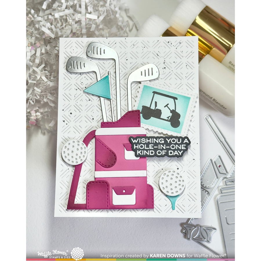A handmade greeting card featuring a golf-themed design with a pink and white golf bag, golf clubs, golf balls, a teal flag, and a golf cart graphic. The card has a white textured background and a black banner that reads, 'WISHING YOU A HOLE-IN-ONE KIND OF DAY.