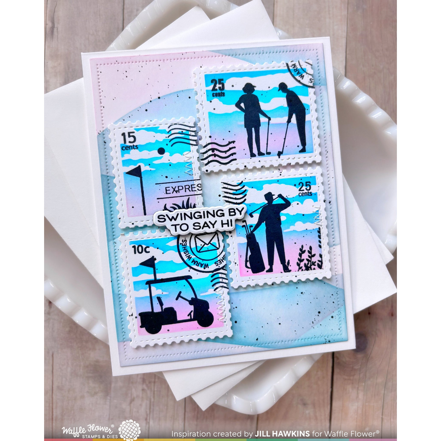 A handmade greeting card featuring golf-themed postage stamp illustrations, displayed on top of white folded paper over a light wood surface. The stamp design includes silhouettes of golfers, a golf cart, and golf course elements in black, blue, white, and soft pink.