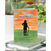 A handmade greeting card featuring a golf-themed retirement design, displayed on top of a speckled golf-themed notebook with blurred plants in the background.