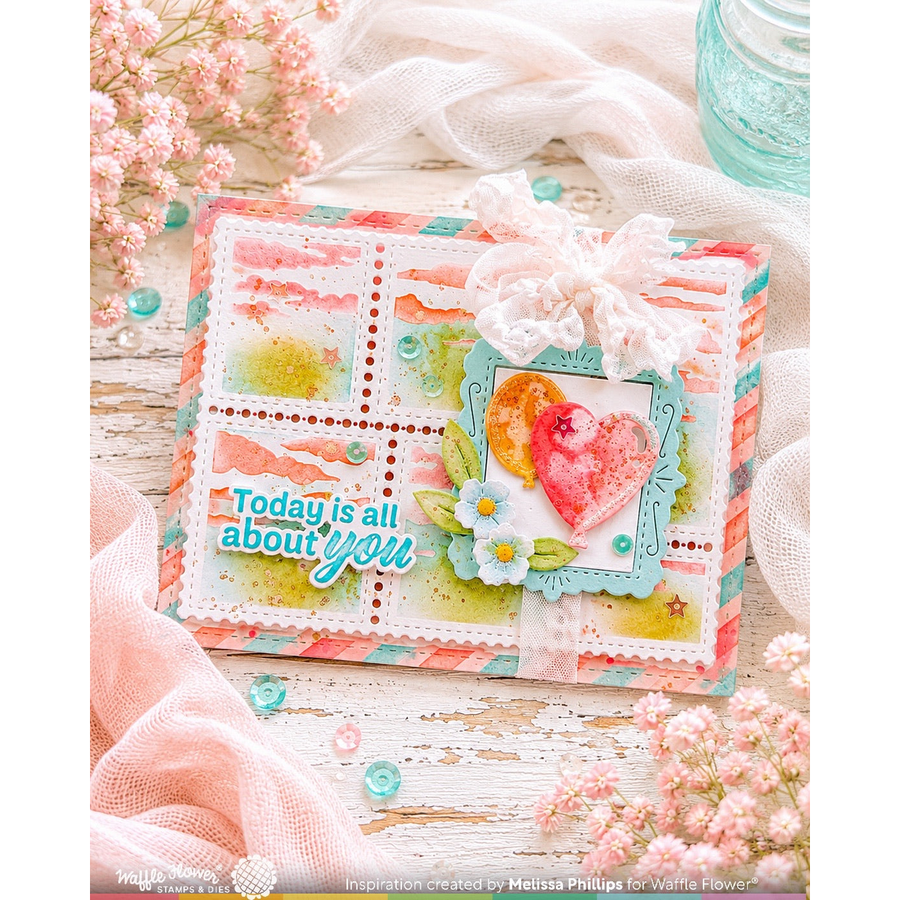 A handmade greeting card or scrapbook card featuring a pastel watercolor design with pink, peach, and blue sections, a white lace bow, a heart embellishment, and the phrase 'Today is all about you' in blue and white lettering. The card is styled on a rustic white wooden surface with pink fabric, small flowers, and decorative elements.