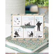 A rectangular fishing-themed birthday card displayed on top of a floral-patterned notebook. The card features six postage-stamp-like panels with black fishing silhouettes on a pale sky background and the text 'HOPE YOUR BIRTHDAY IS OFF THE HOOK' plus 'FISHING' and 'FOREVER'.