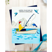 A handmade greeting card featuring a whimsical fishing scene with a person in a boat on blue water, with mountains and birds in the background. The card reads 'HOPE YOUR DAY IS SMOOTH SAILING.