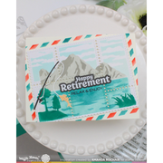 A handmade retirement-themed greeting card displayed on a white pearl-edged plate. The card features a mountain lake landscape with a fishing rod and a yellow fish, alongside the text 'Happy Retirement RELAX & ENJOY'.