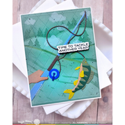 A handmade greeting card featuring a fishing theme, displayed on top of white envelopes over a light wood background. The card has a teal-green background with a diamond-stamped texture, showing a blue fishing rod, a green and yellow fish, and a hand holding the rod.