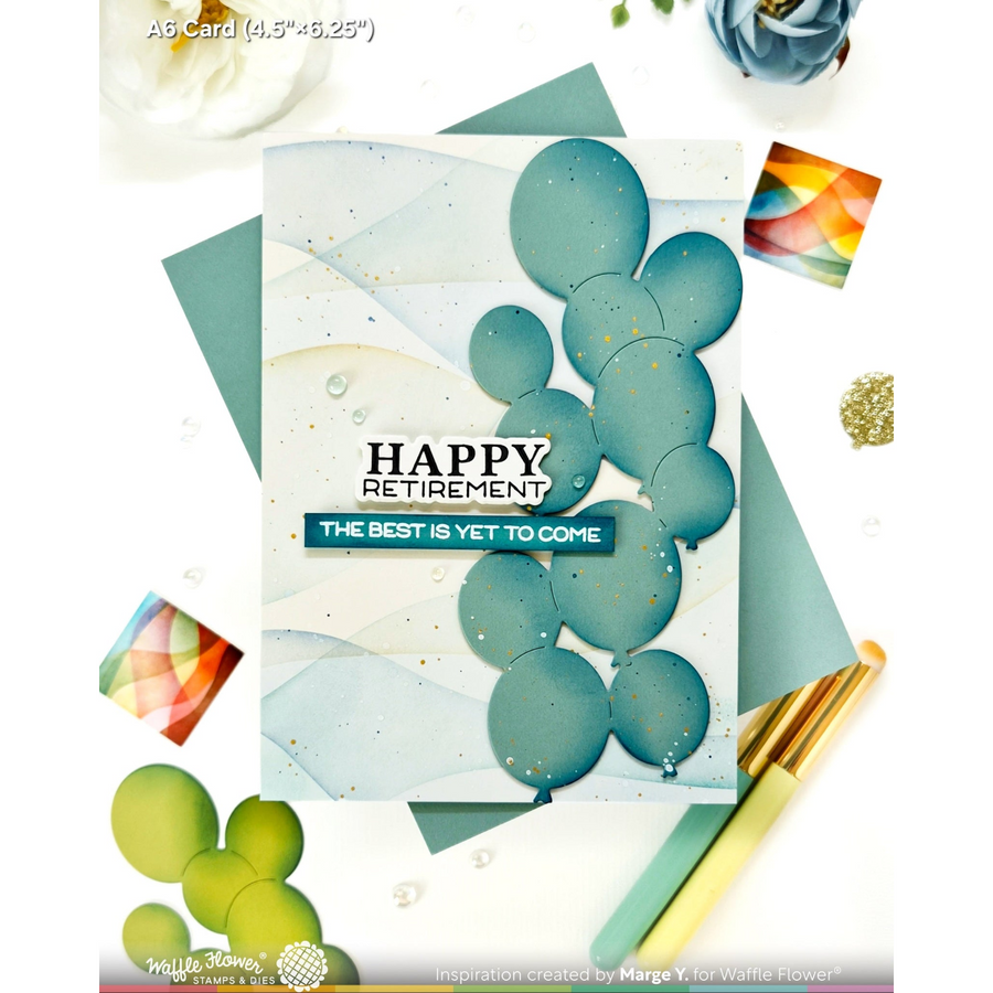A handmade retirement greeting card with layered teal and blue balloon shapes and the text 'HAPPY RETIREMENT' and 'THE BEST IS YET TO COME,' styled on a white background with envelopes, flowers, and decorative cards.