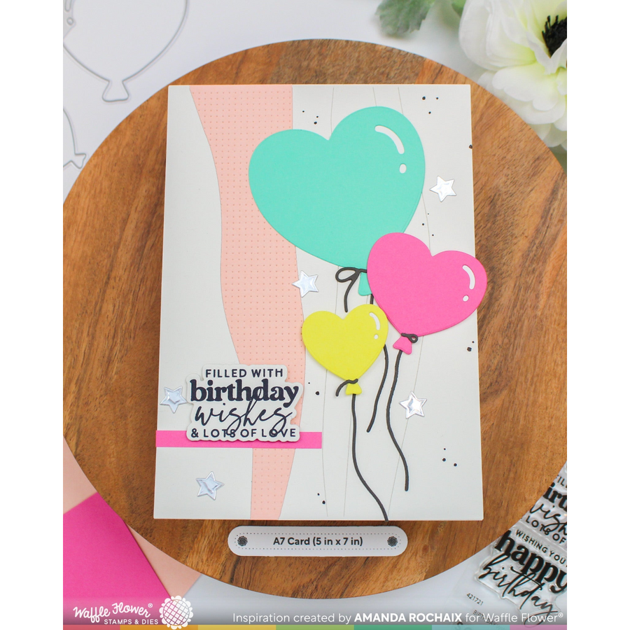 A handmade greeting card with three heart-shaped balloons in mint green, pink, and yellow, displayed on a round wooden board. The card features the text 'FILLED WITH birthday wishes & LONG OF LOVE' and is branded with Hello Stamp.