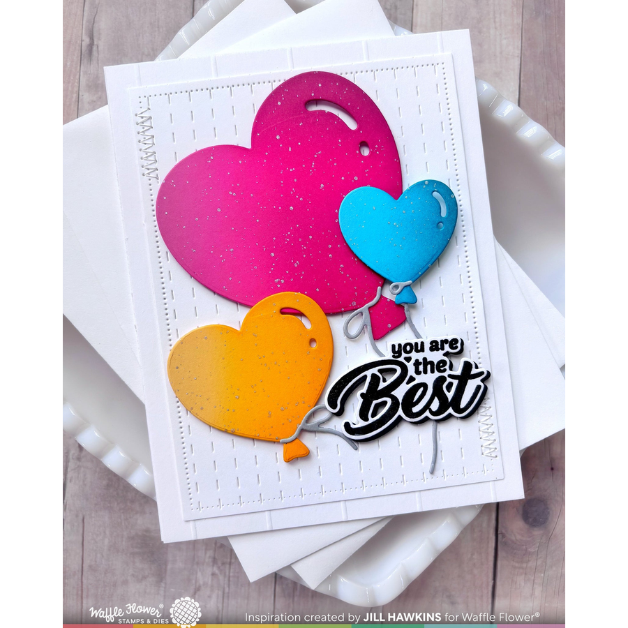 A handmade greeting card featuring three glittery heart-shaped balloons in pink, blue, and orange, with the text 'you are the Best' in black script, displayed on stacked white cards over a light wood background.